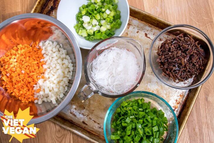 Ingredients for vegan steamed buns on in separate bowls on a baking tray (carrot, jicama, onion, mung bean vermicelli, and wood ear mushroom)