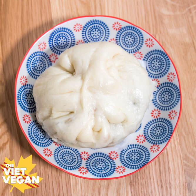 A cooked steam bun on a blue and white plate with a pink edge.