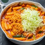 large saute pan with rabokki, topped with shredded cabbage