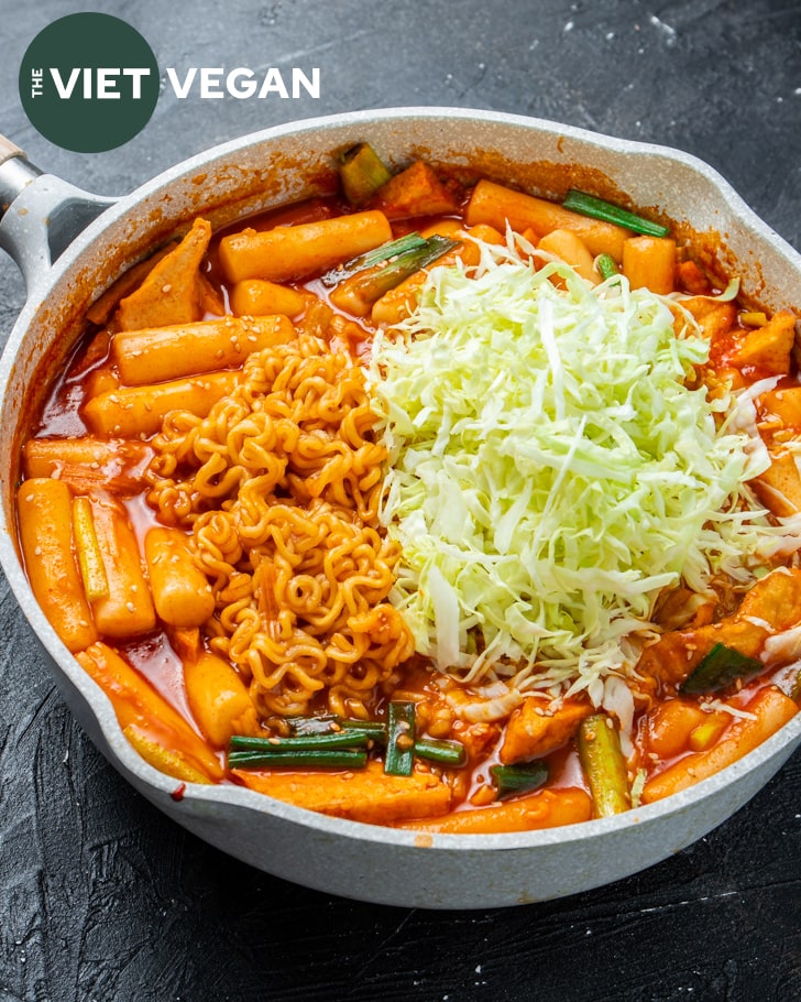 large saute pan with rabokki, topped with shredded cabbage