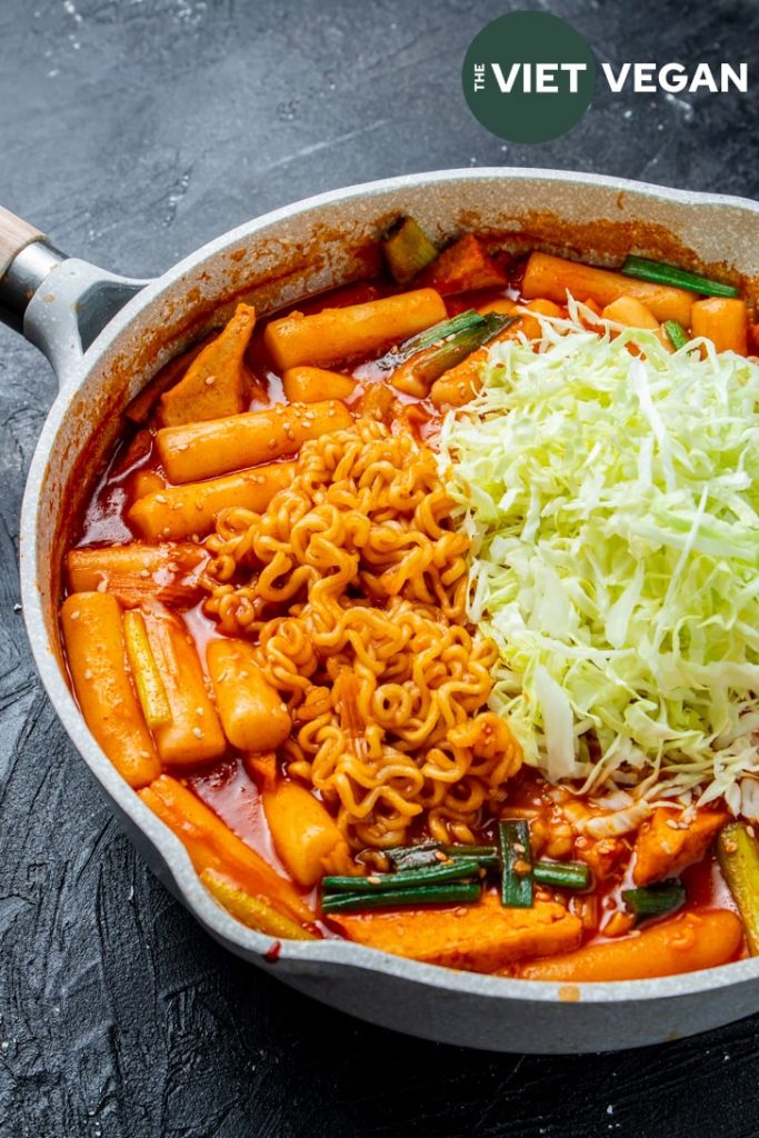 vegan rabokki (tteokbokki with ramen) in a saute pan with shredded cabbage on top