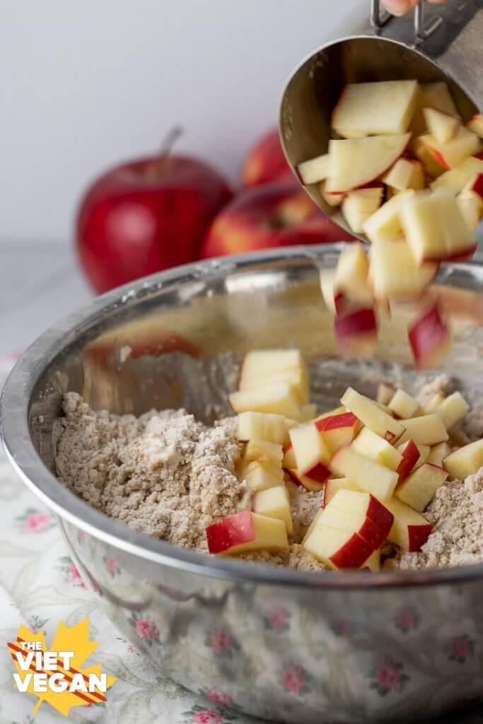 Apples falling from a measuring cup onto batter