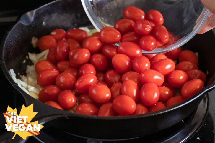 pouring cherry tomatoes into a cast iron skillet