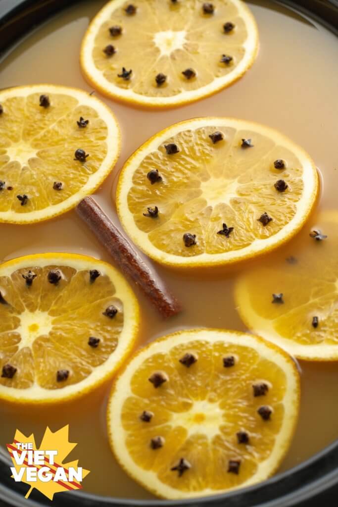 Orange slices pierced with cloves and cinnamon floating in apple cider