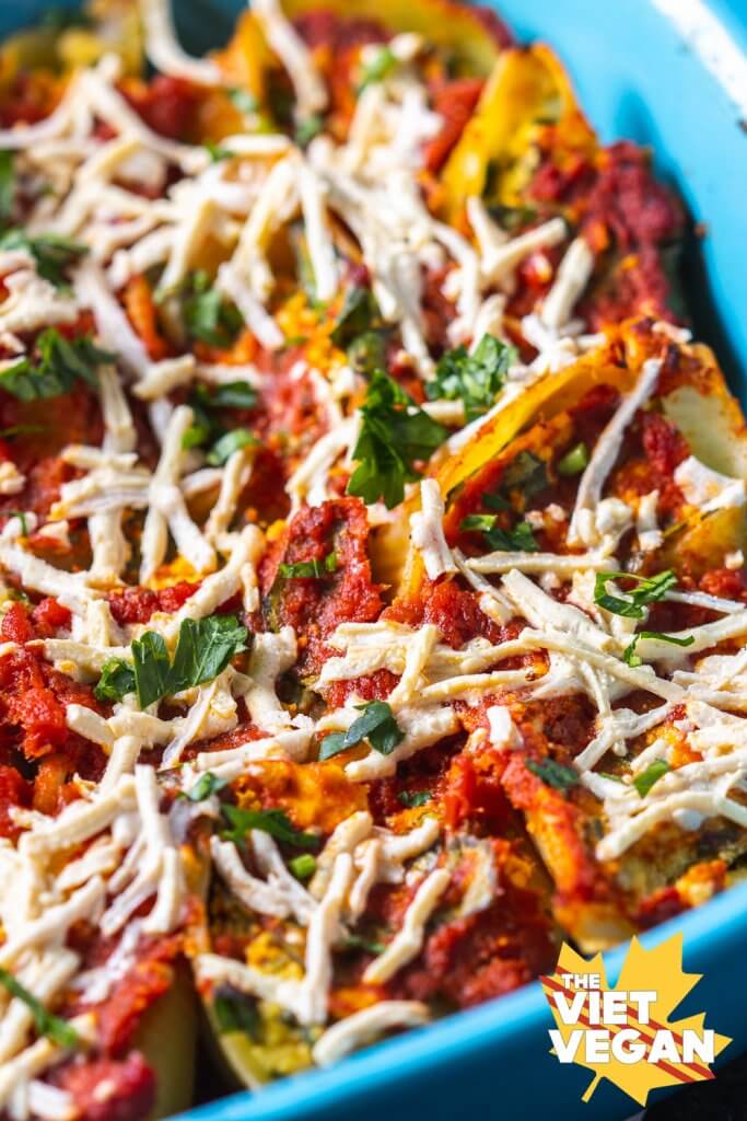 Close up of tofu ricotta stuffed shells in a baking pan topped with sauce and vegan cheese