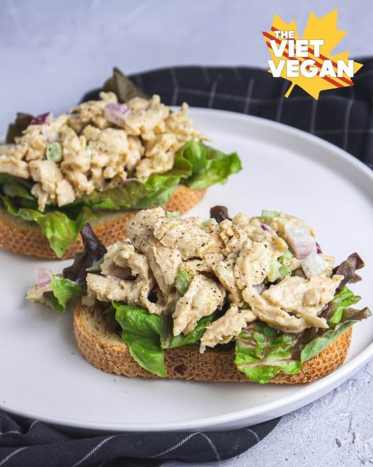 Two vegan chicken salad open faced sandwiches, on a plate with a napkin