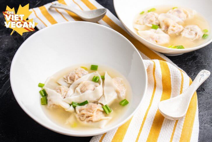 vegan wonton soup in bowls, on a yellow and white kitchen towel, with a spoon