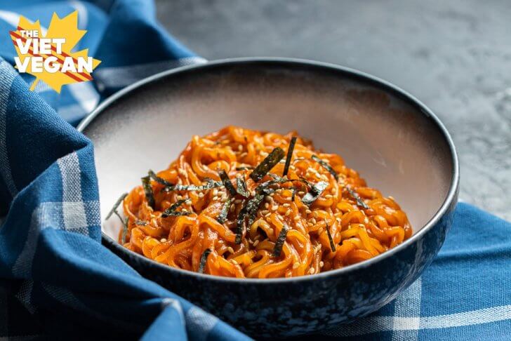 red ramen noodles topped with sesame and nori in a bowl, set on a blue kitchen cloth on a black surface, from the front