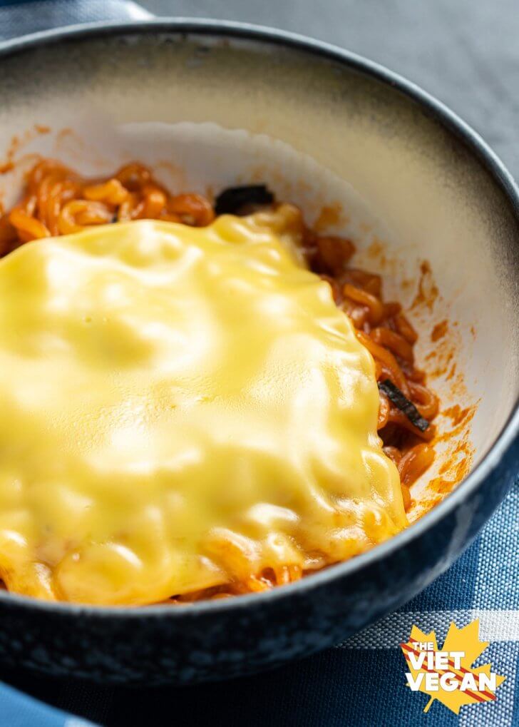 red fire noodles in a bowl topped with a slice of melted american-style cheese