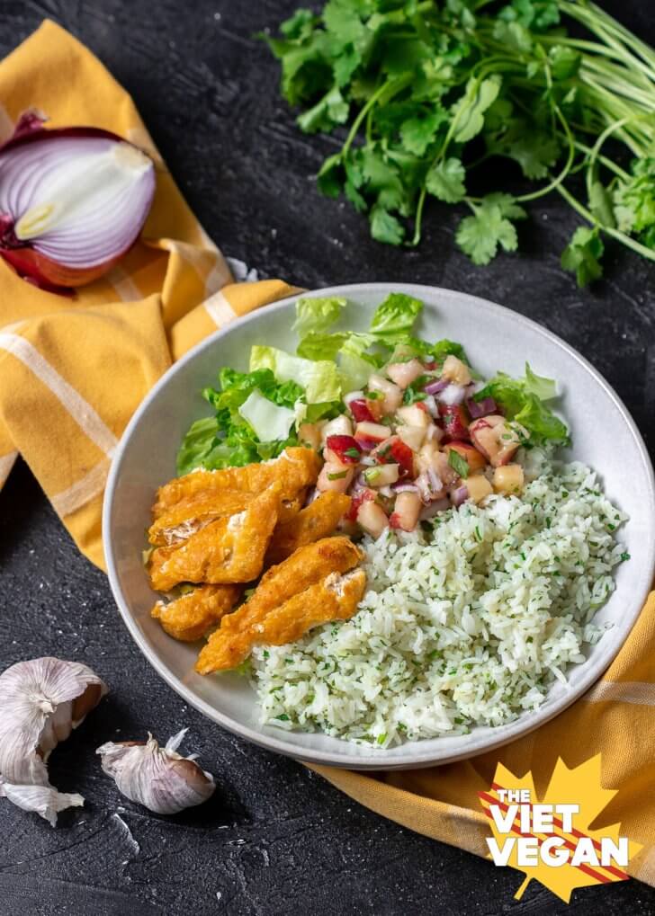 bowl filled with cilantro rice, sliced vegan fish, lettuce, and a peach salsa