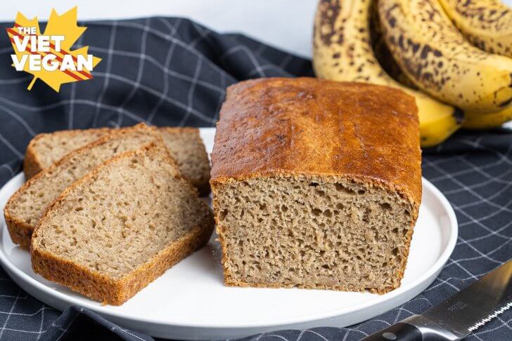 vegan sourdough banana bread, sliced and displayed on a white plate, on a black grid-pattern tea towel, from a front angle