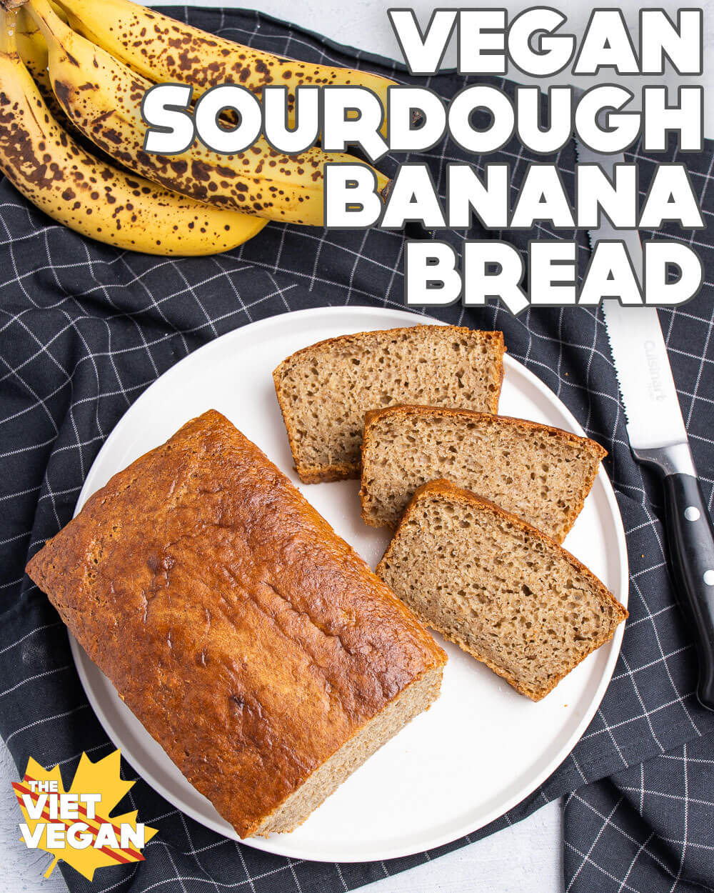 vegan sourdough banana bread, sliced and displayed on a white plate, on a black grid-patterned tea towel, with overripe bananas and a bread knife