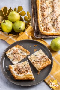 Three slices of the tart on a plate, on a yellow tea towel with the baked tart in the background and green California Bartlett pears beside them