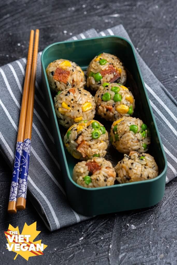 Close up of 8 onigiri in the bento box layer, on top of a striped grey napkin with chopsticks