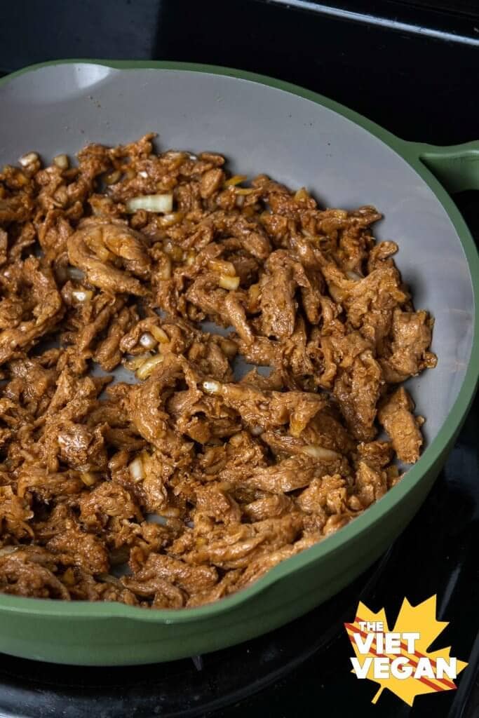 soy curls cooking in a grey and green non-stick pan