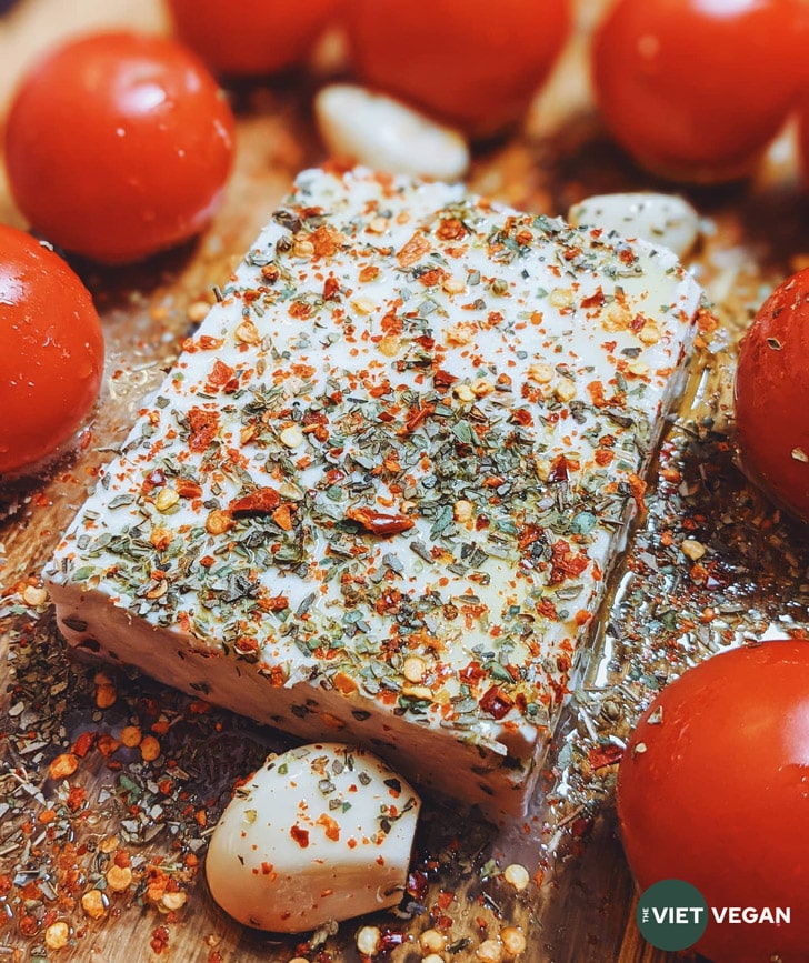 feta in a casserole dish, surrounded by tomatoes and garlic, sprinkled with herbs and spices and olive oil