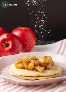 apple pie pancakes with apples in background and dusting of icing sugar