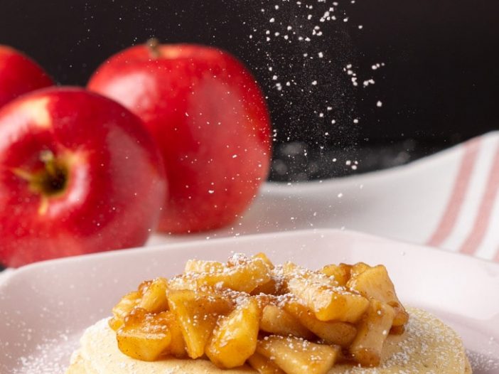 apple pie pancakes with apples in background and dusting of icing sugar