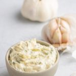 garlic butter in a small bowl, with a full head of garlic and a half head in the background