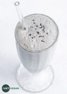 black sesame milkshake in large milkshake glass with a glass straw, garnished with black sesame seeds