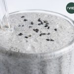 close up of black sesame milkshake in large milkshake glass with a glass straw, garnished with black sesame seeds