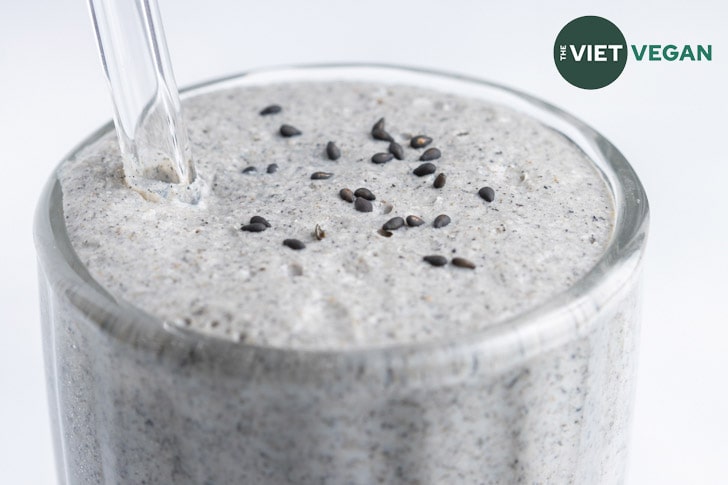 close up of black sesame milkshake in large milkshake glass with a glass straw, garnished with black sesame seeds