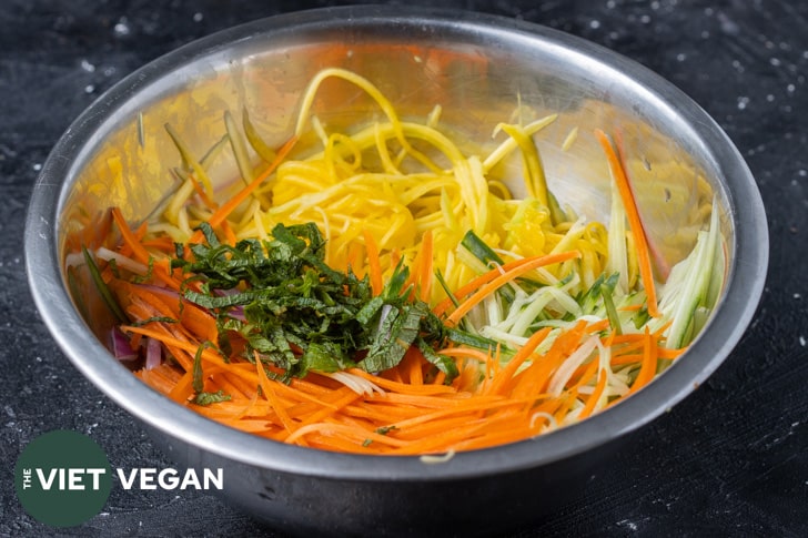 Large mixing bowl with julienned green mango, mint, carrot, red onion, and cucumber