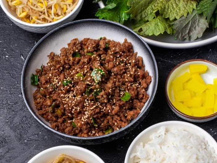 ingredients for ssam with bulgogi ground, japchae, kongnamul muchim, rice and pickled radish in bowls