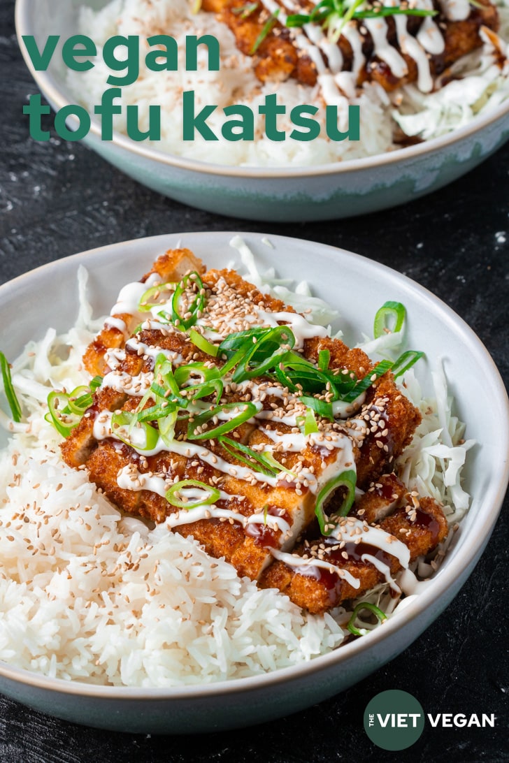 Vegan Tofu Katsu in a bowl drizzled with tonkatsu sauce, vegan mayo, scallions, sesame seeds, on a bed of shredded cabbage and rice