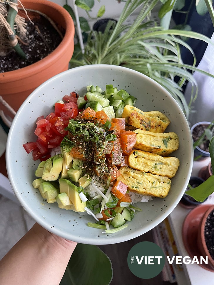 Vegan poke bowl filled with tomatoes, avocado, vegan salmon poke, cucumber, and vegan tamagoyaki over a bed of rice