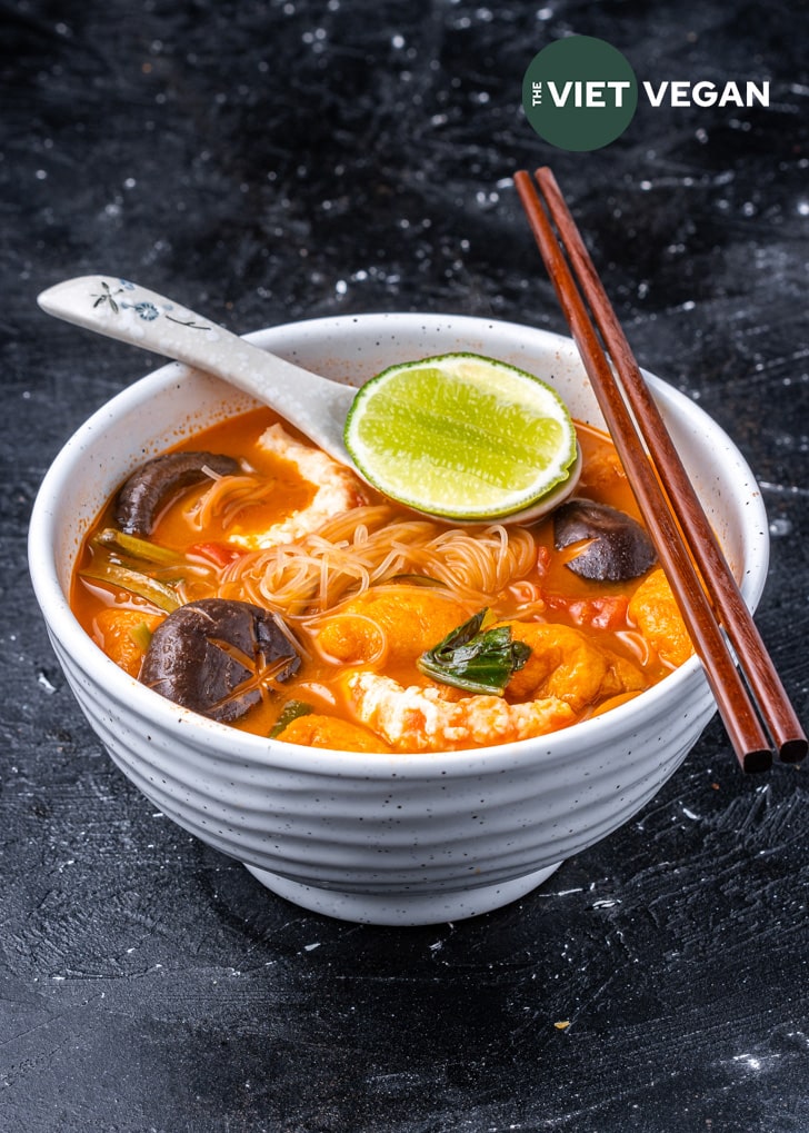 A side angle of tom yum noodle soup in a large soup bowl on a dark, uneven textured background