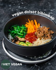 Rice with vegetable side dishes arranged on top in a ceramic bowl with bibimbap sauce in the middle