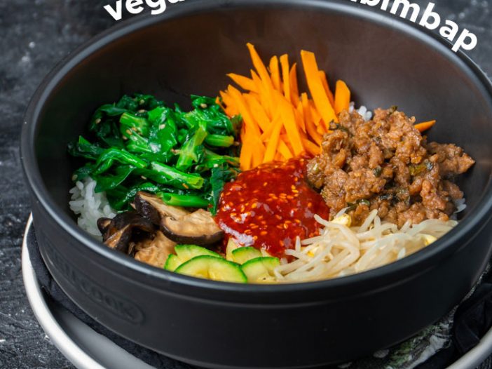 Rice with vegetable side dishes arranged on top in a ceramic bowl with bibimbap sauce in the middle