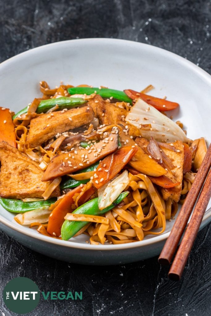 Vietnamese stir fried chow mein (mi xao chay) in a bowl with chopsticks on a dark surface