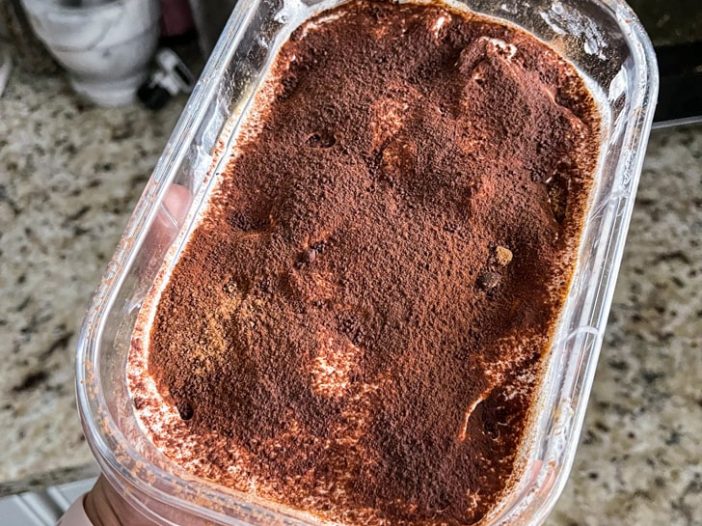 Container of vegan biscoff tiramisu, top layer view of dusted cocoa powder