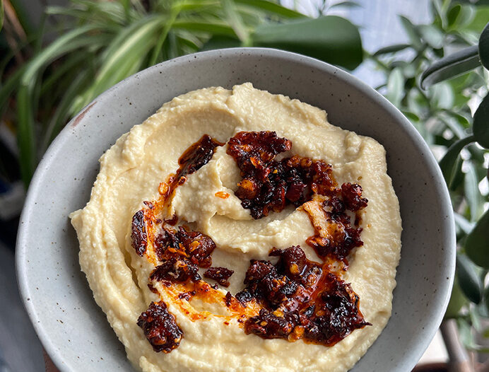 The creamiest hummus in a serving bowl with chili crisp on top