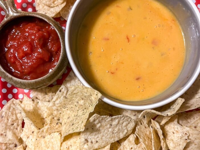 vegan queso in a bowl beside salsa, surrounded by tortilla chips