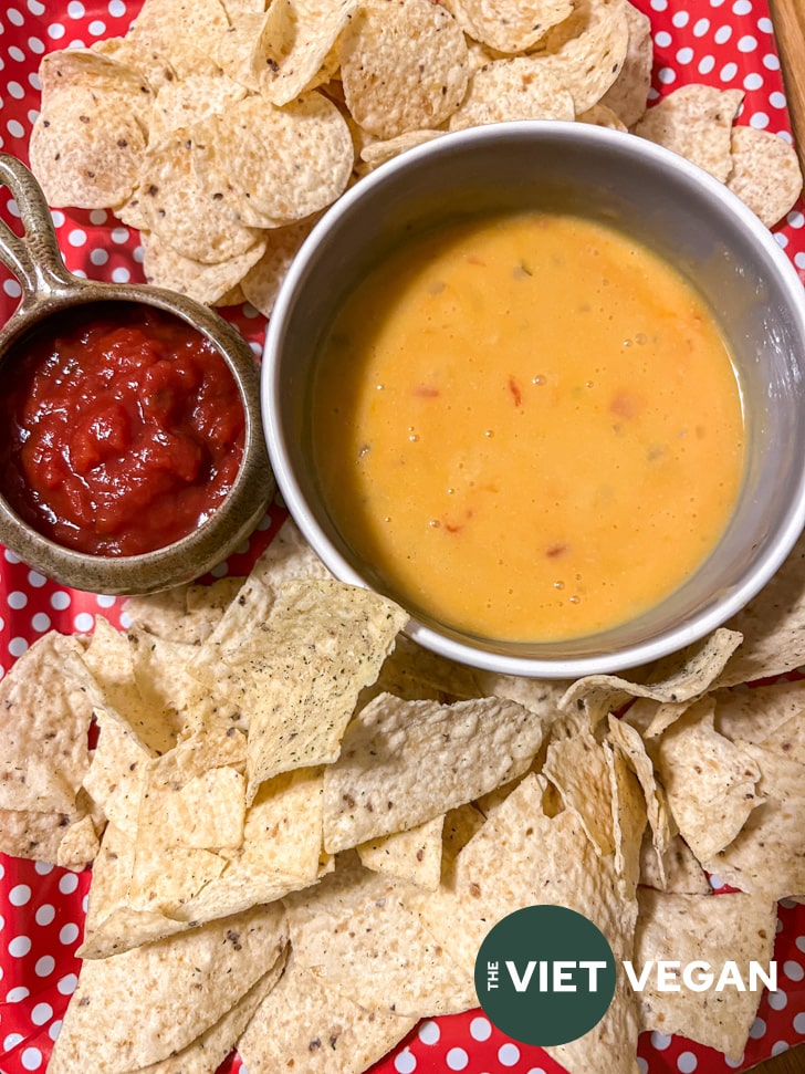 vegan queso in a bowl beside salsa, surrounded by tortilla chips
