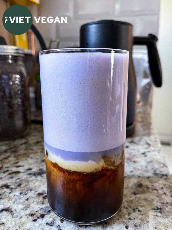 a glass of vietnamese iced coffee with a layer of oat cream and ube foamed milk