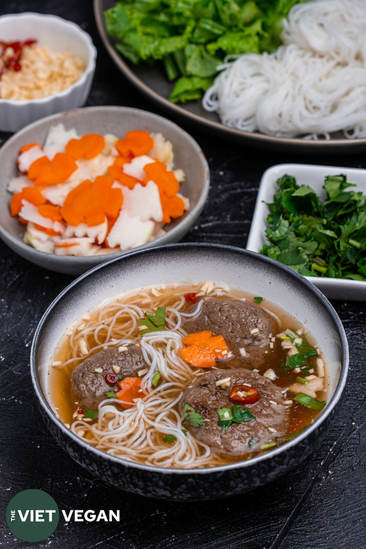 bowl with dipping sauce, with impossible chả chay, noodles, and toppings in the bowl, Bowls of the toppings in the background