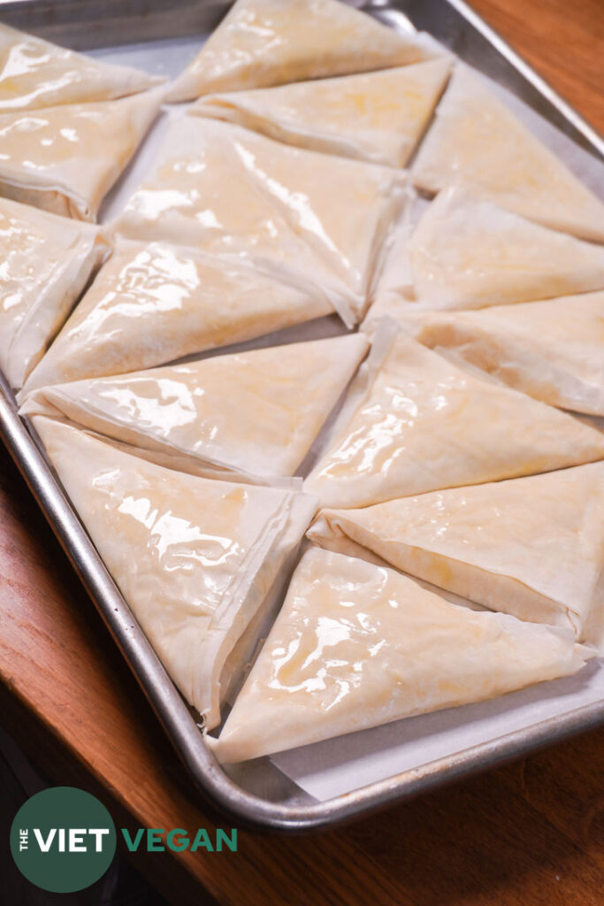 a baking tray covered in a single layer of assembled spanakopita triangles before baking