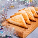vegan spanakopita triangles on a cutting board surrounded by snowflake tinsel