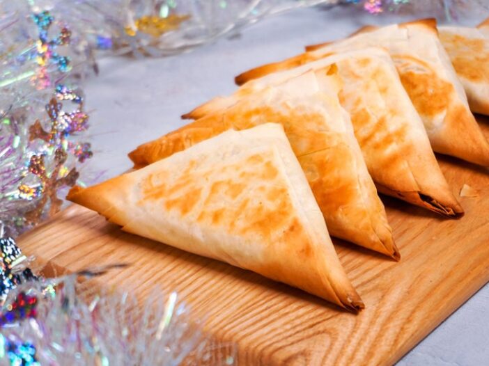 vegan spanakopita triangles on a cutting board surrounded by snowflake tinsel