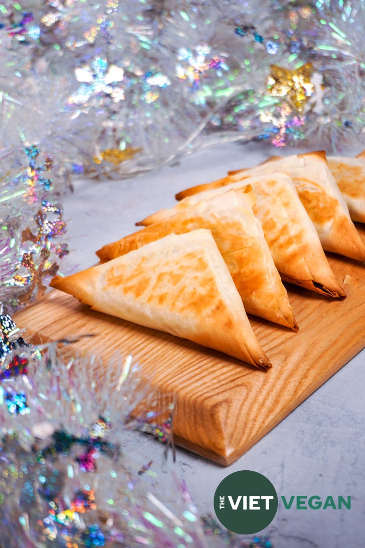 vegan spanakopita triangles on a cutting board surrounded by snowflake tinsel