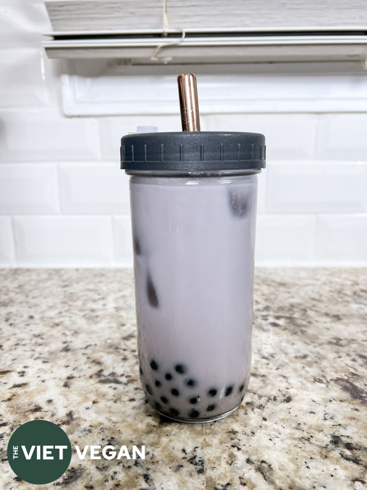 vegan taro milk bubble tea in a glass reuseable cup with black tapioca pearls.