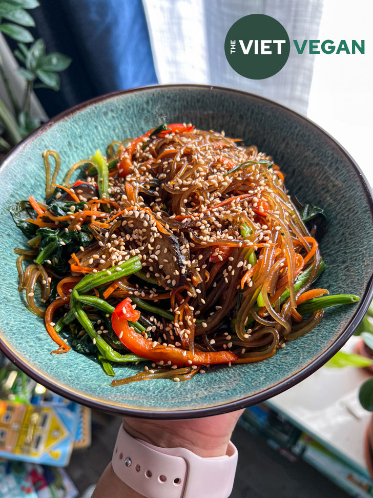 japchae noodles in a green bowl with sesame seeds on top