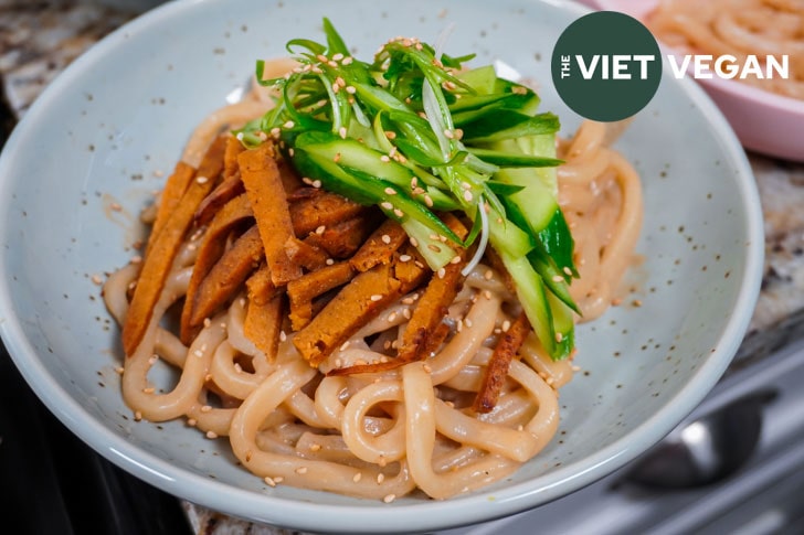 sesame udon topped with sliced seitan, cucumber, and green onion curls, horizontal orientation