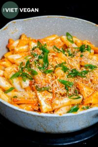 rabokki carbonara in a pan with spring onion and toasted sesame seeds on top
