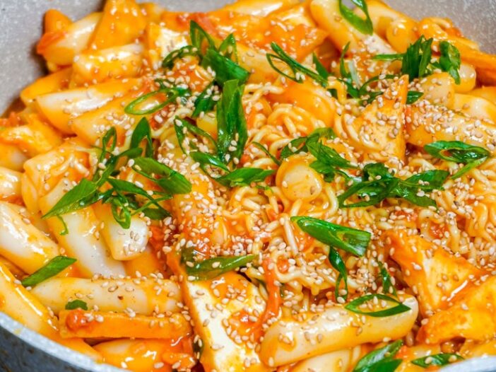 rabokki carbonara in a pan with spring onion and toasted sesame seeds on top
