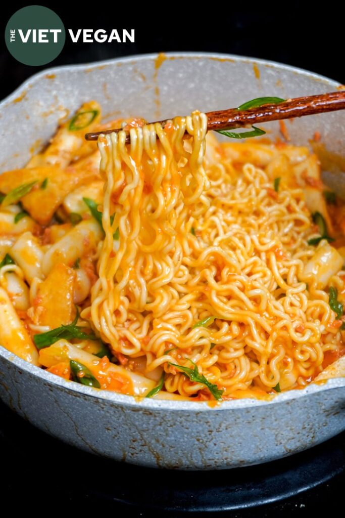 ramen noodles in chopsticks over a pan of rabokki carbonara